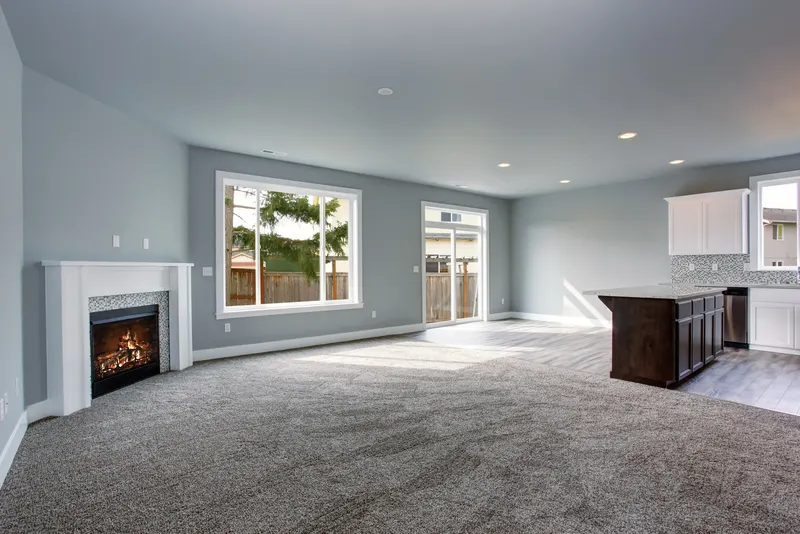 An empty living room with a fireplace and clean gray carpet